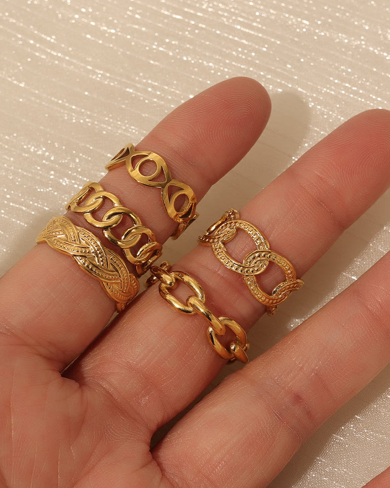 Mano con varios anillos dorados de eslabones de distintos tamaños y acabados, sobre fondo claro.