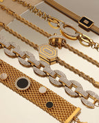 Varias pulseras doradas sobre una superficie reflectante, con diseños de cadenas, lazos y círculos negros.