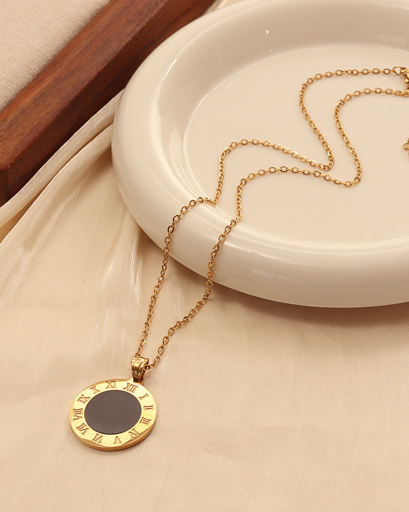 Collar dorado con medallón circular de centro negro y borde con números romanos, junto a un plato blanco.