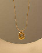 Collar dorado con colgante ovalado irregular de centro hundido y brillante, suspendido sobre fondo beige.