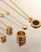 Varias joyas doradas sobre espejo, con colgantes redondos de centro negro y anillo ancho de bandas decoradas.