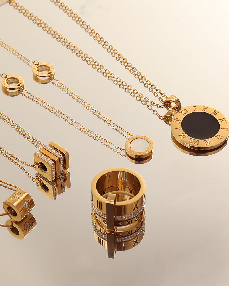 Varias joyas doradas sobre espejo, con colgantes redondos de centro negro y anillo ancho de bandas decoradas.