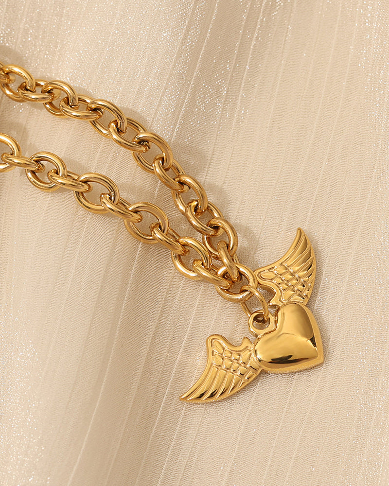 Detalle de collar dorado de eslabones ovalados y colgante de corazón con alas extendidas, sobre fondo claro.