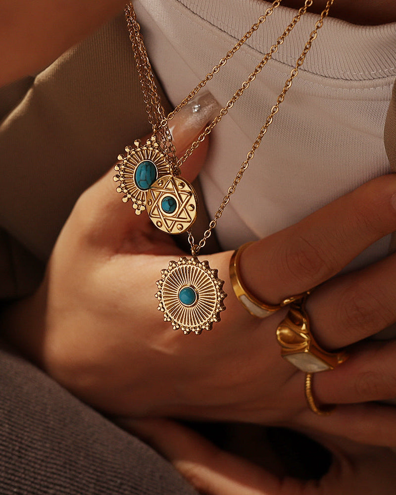 Persona con varios collares dorados de medallones, dos con centro azul turquesa, y anillos dorados.