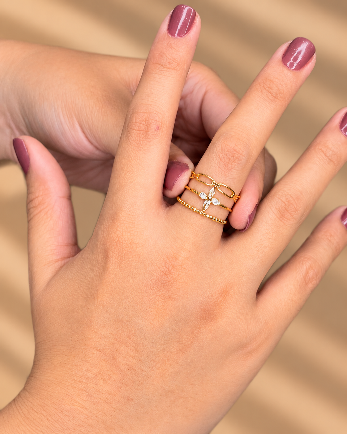Anillo dorado de varias bandas finas con pequeños motivos geométricos, puesto en una mano con uñas moradas.