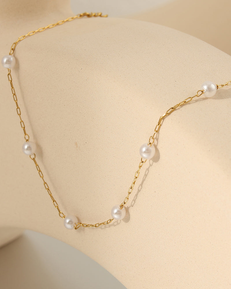 Tobillera de dos cadenas finas doradas con pequeñas perlas blancas, extendida sobre soporte beige.