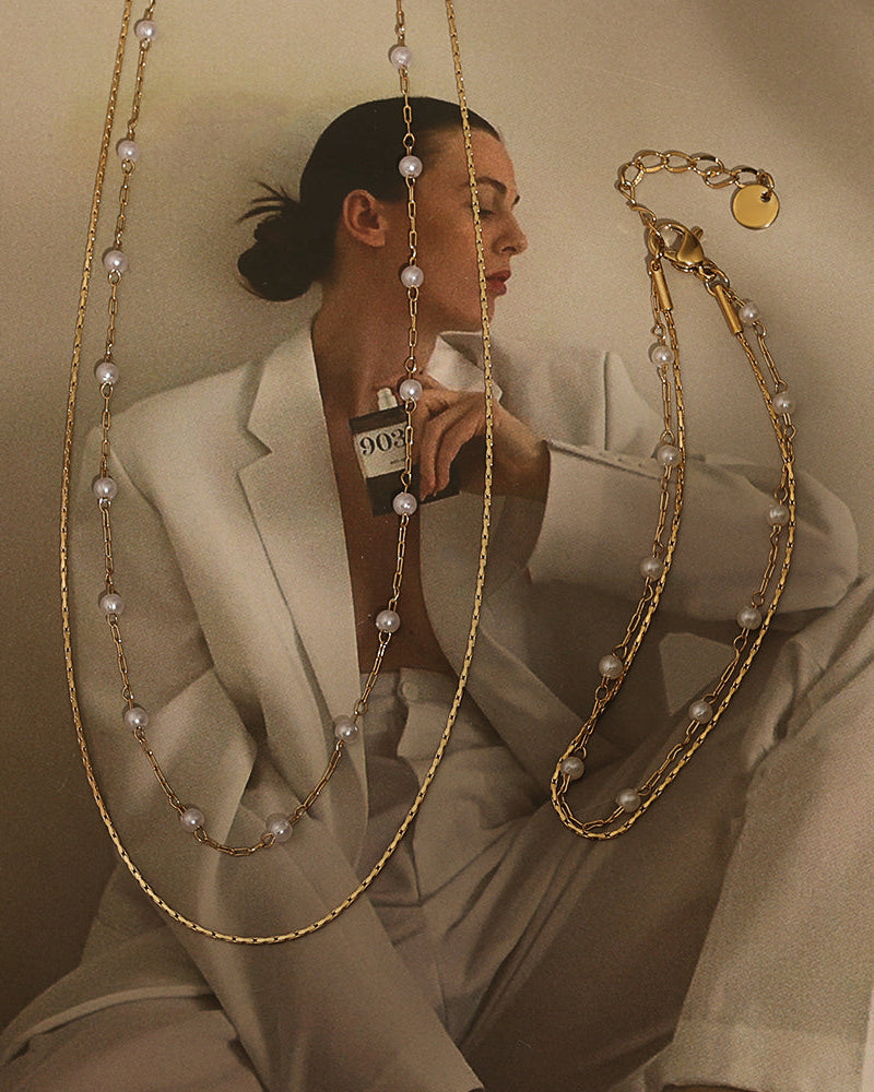Dos collares dorados largos, uno con pequeñas perlas blancas, sobre una fotografía de una mujer con traje claro.