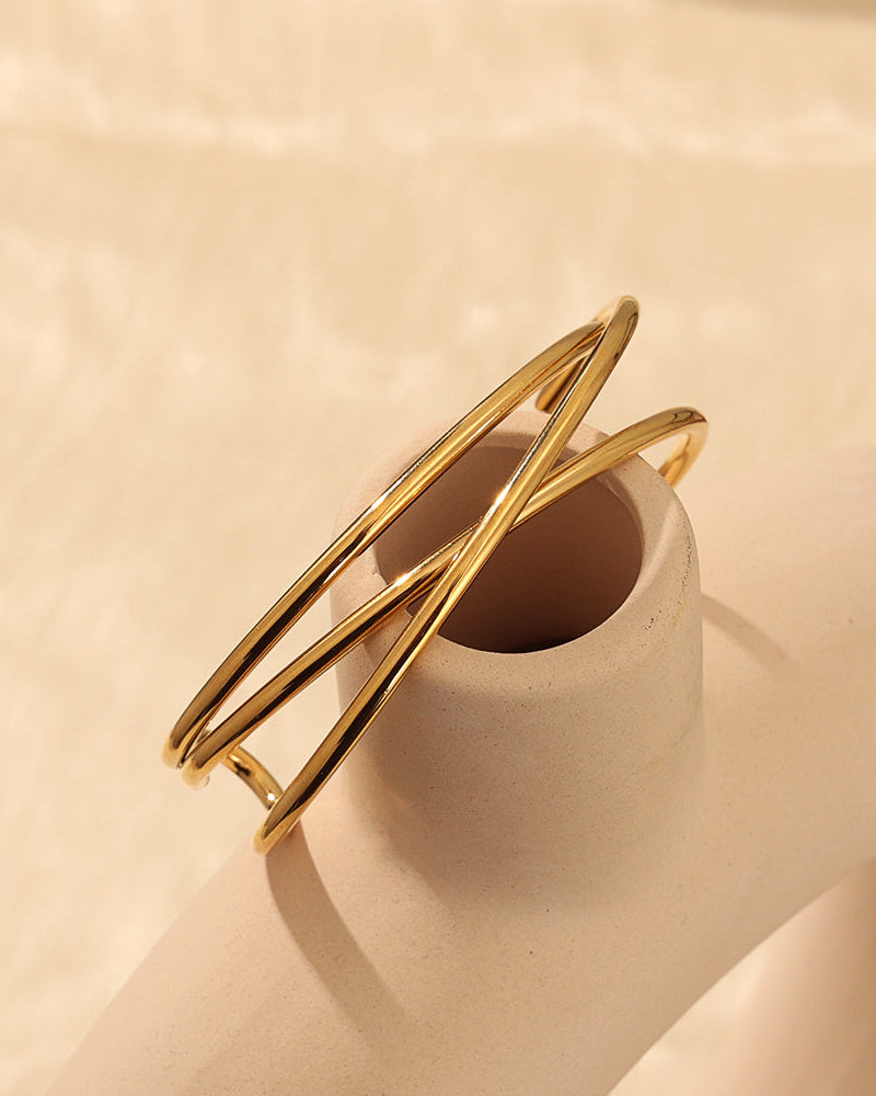 Pulsera rígida dorada de varios aros finos cruzados, apoyada sobre un pequeño recipiente beige.