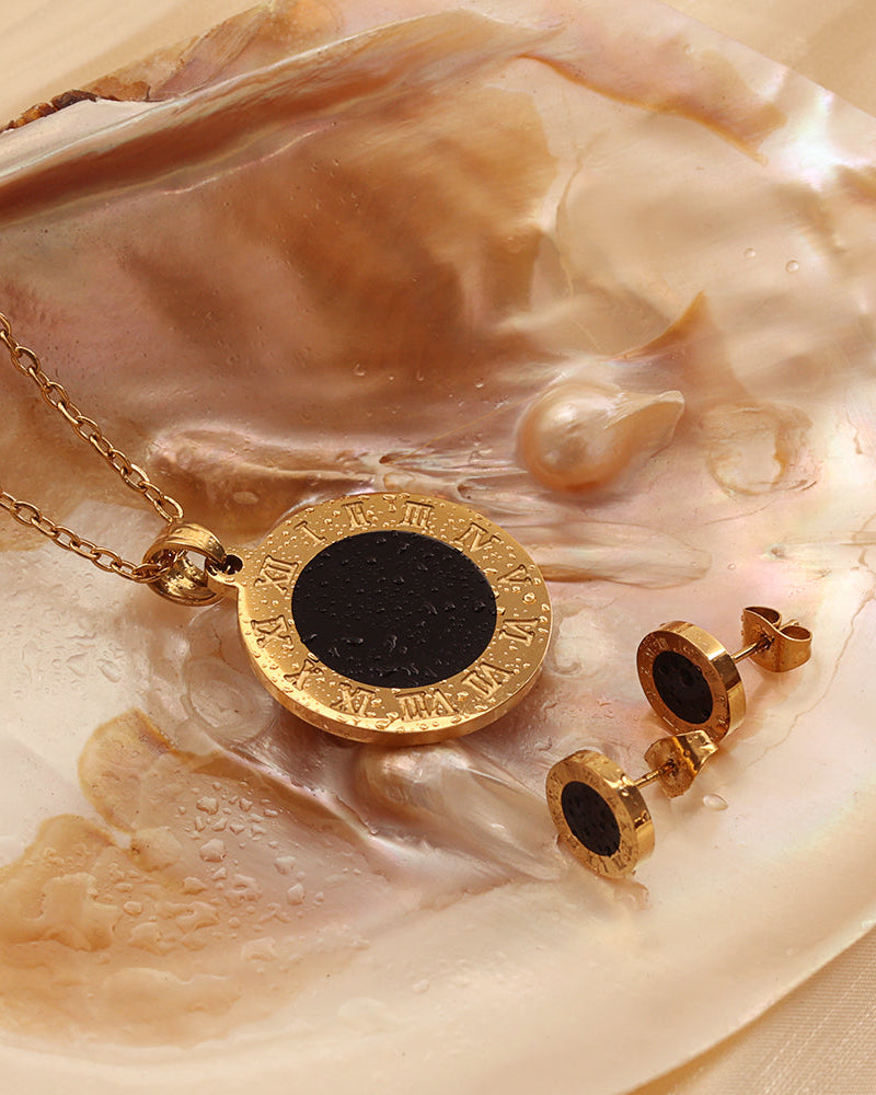 Collar y pendientes dorados de motivos redondos negros y bordes grabados, sobre una concha de tonos crema.