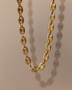 Collar dorado de eslabones ovalados gruesos, suspendido sobre fondo beige con sombra lateral.