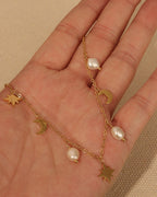 Collar dorado con pequeñas perlas blancas y colgantes de estrellas y medias lunas, extendido sobre una mano.