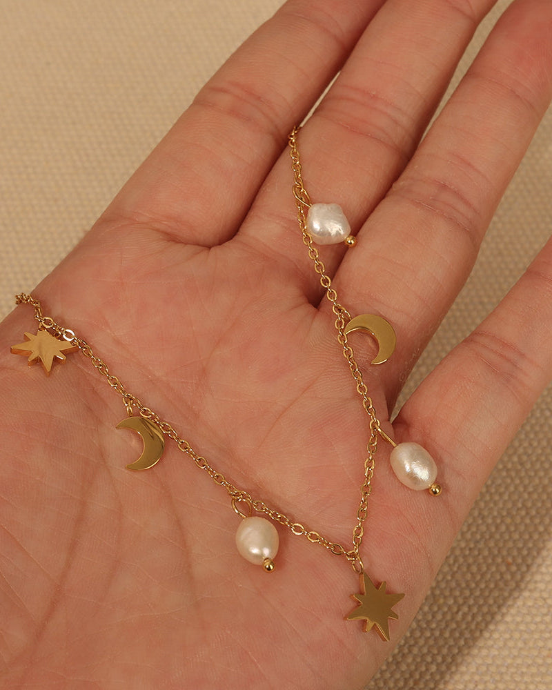 Collar dorado con pequeñas perlas blancas y colgantes de estrellas y medias lunas, extendido sobre una mano.