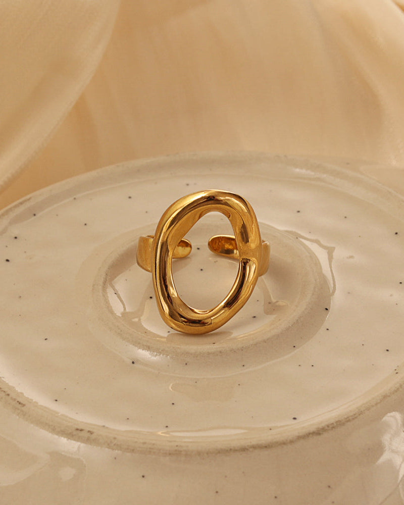 Anillo dorado de gran óvalo abierto y bordes redondeados, sobre un plato de cerámica claro.