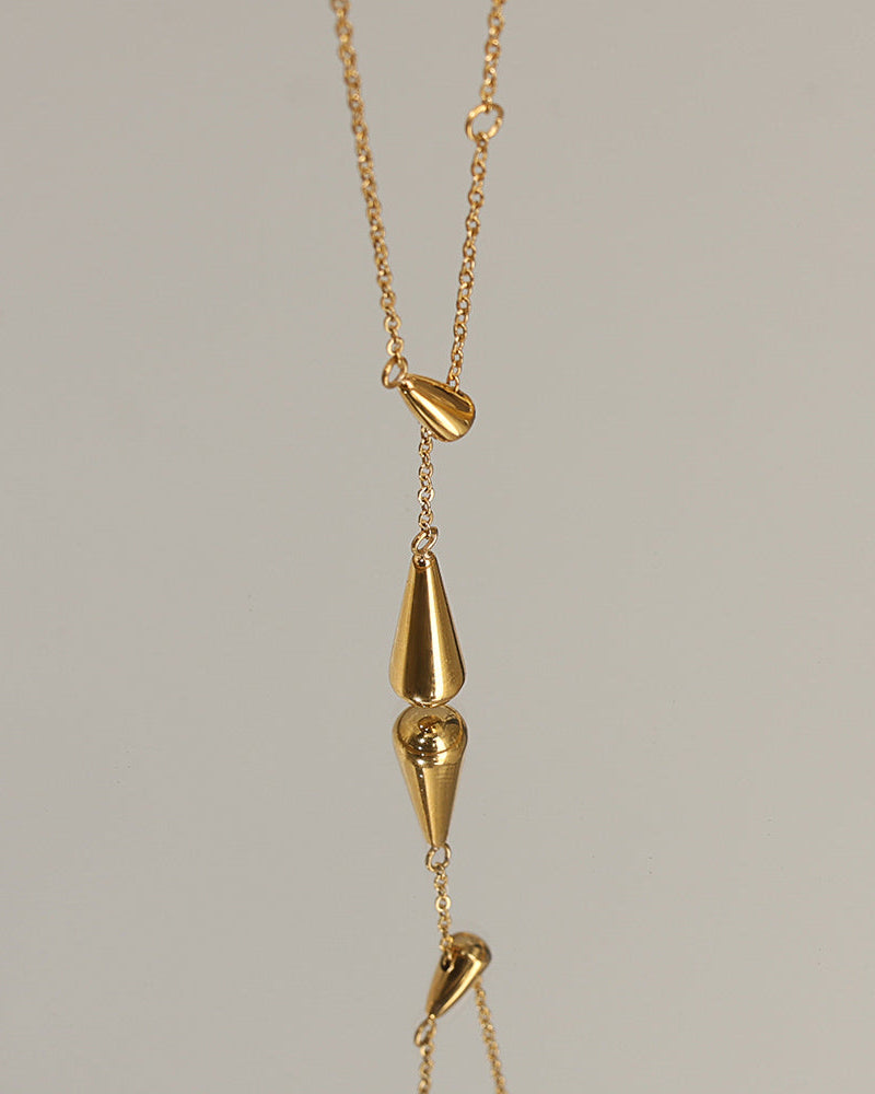 Detalle del collar dorado con colgantes alargados en forma de gota, suspendido sobre fondo claro.
