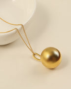 Collar de cadena fina dorada con colgante esférico grande y liso, junto a un plato blanco.