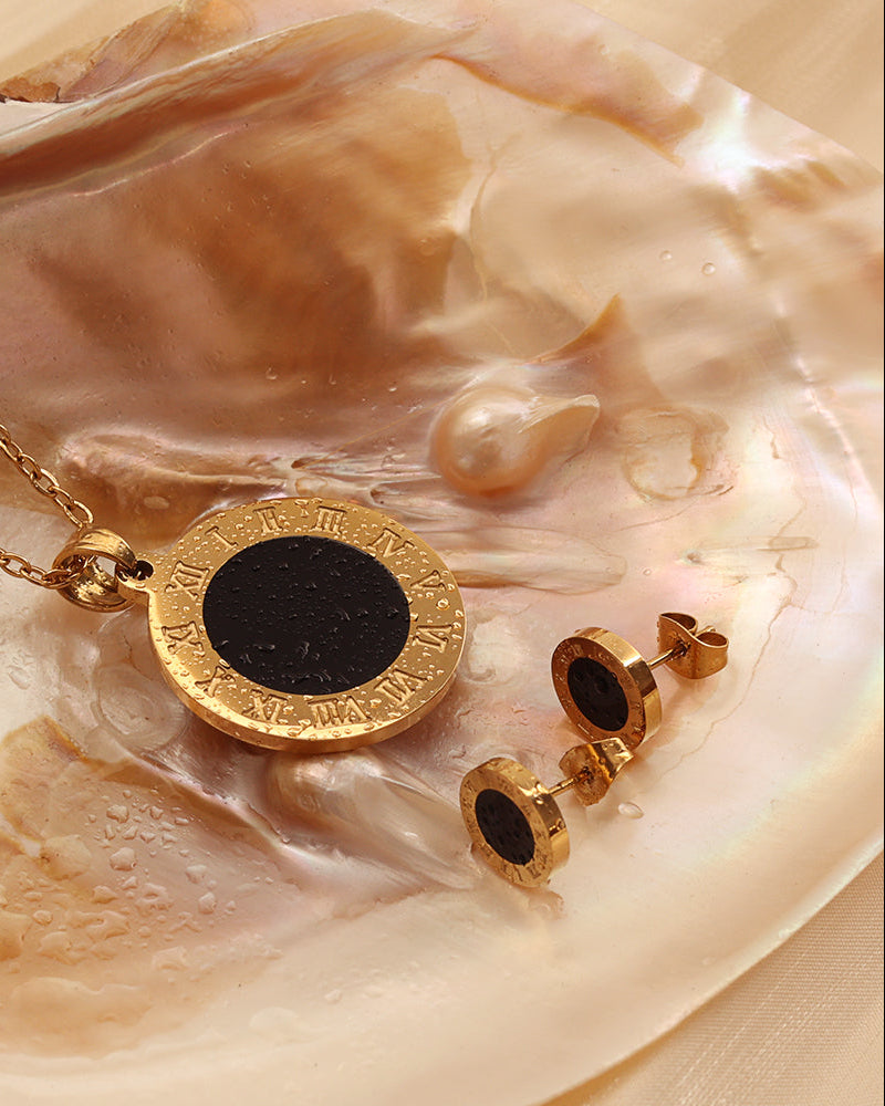 Collar y pendientes de discos negros con bordes dorados grabados, colocados sobre una concha.