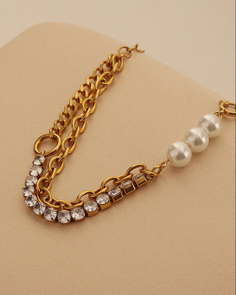 Pulsera dorada con eslabones, pequeñas piedras claras y perlas blancas, extendida sobre un soporte beige.