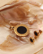 Collar y pendientes de discos negros con marcos dorados grabados, sobre una concha.