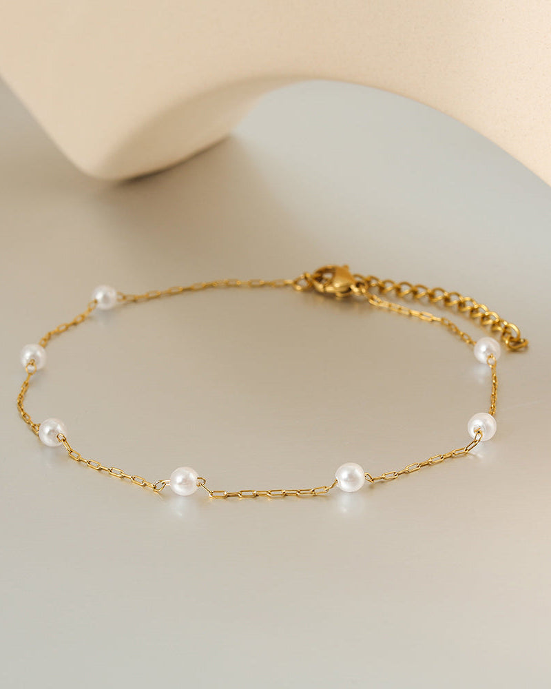 Tobillera fina dorada de dos cadenas con pequeñas perlas blancas y extensión, sobre superficie clara.