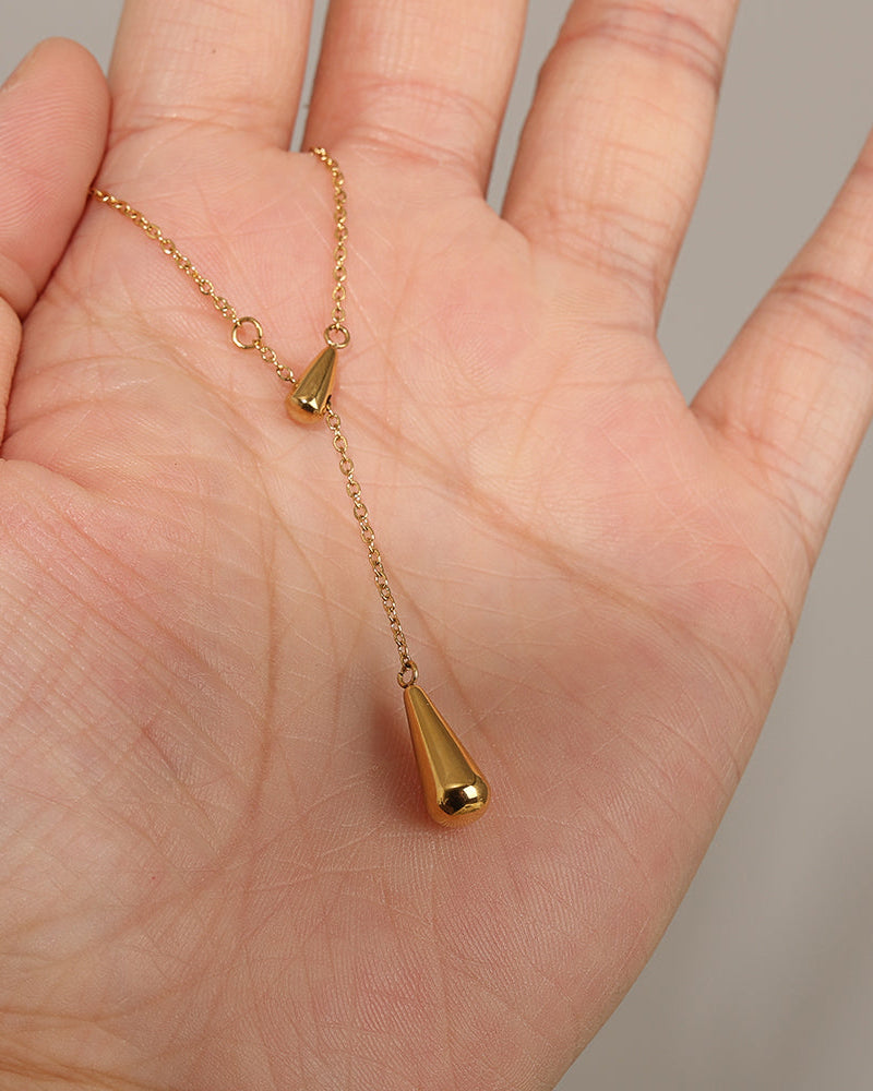 Collar fino dorado con dos colgantes en forma de gota, extendido sobre la palma de una mano.