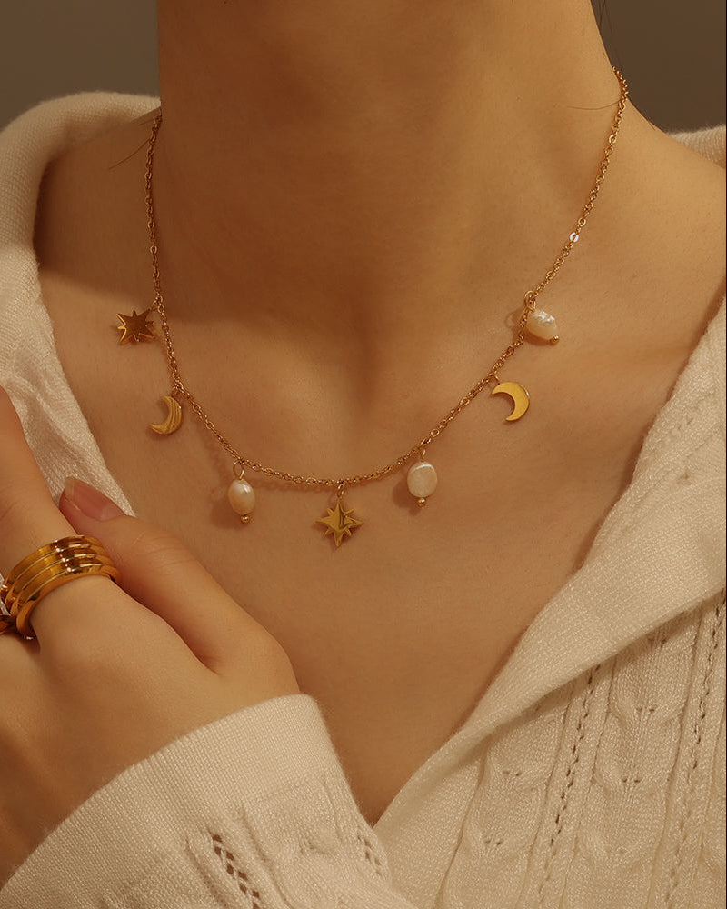 Persona con collar fino dorado de perlas blancas y colgantes de estrellas y medias lunas, sobre blusa clara.