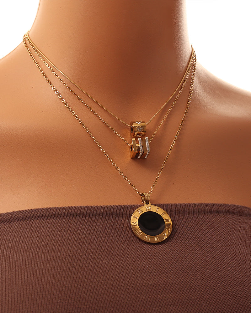 Persona con varios collares dorados superpuestos, con colgantes cilíndrico, geométrico y circular de centro negro.