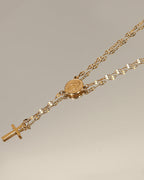 Collar dorado tipo rosario con medalla redonda y cruz colgante sobre superficie clara.