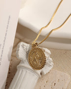 Collar dorado con medallón ovalado de figura en relieve y borde decorado, sobre una pequeña columna blanca.