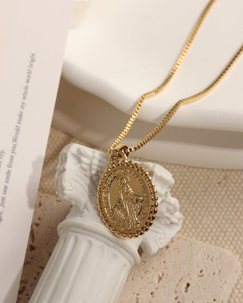 Collar Medallón Albor de Xihe By Dm, con cadena dorada y dije ovalado texturizado con figura en relieve y borde ornamentado, acabado PVD Oro 18K.