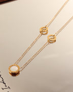 Collar dorado de cadena fina con tres motivos circulares claros y bordes dorados, junto a su reflejo sobre espejo.