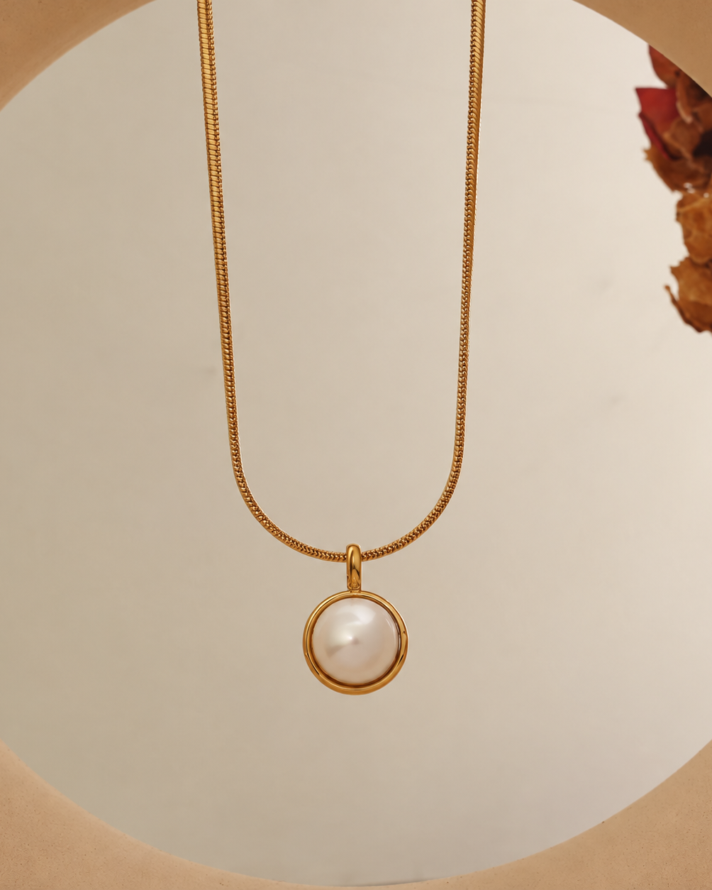 Collar dorado con colgante redondo blanco perlado y borde dorado, suspendido sobre fondo crema.