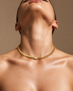 Persona con collar corto dorado que combina cadena plana y eslabones, con la cabeza inclinada hacia atrás.