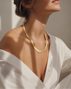 Mujer con collar dorado de cadena plana ancha y camisa blanca abierta.