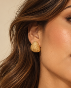 Mujer con pendiente dorado abombado de forma redondeada y textura granulada.