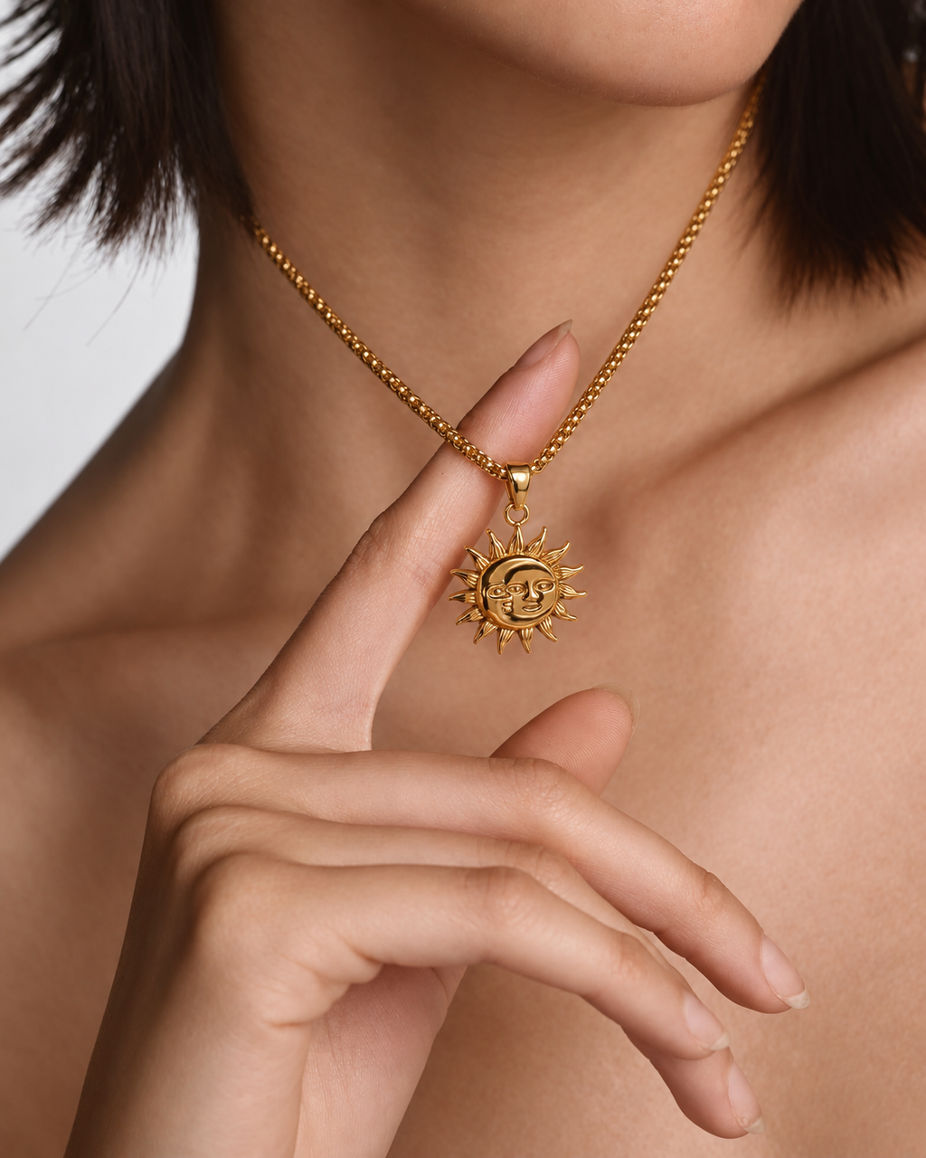 Mujer sosteniendo el colgante dorado de un collar con motivo circular de sol y luna.